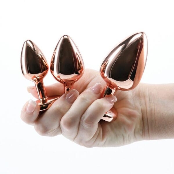 A hand holding three copper cups in front of a white background.