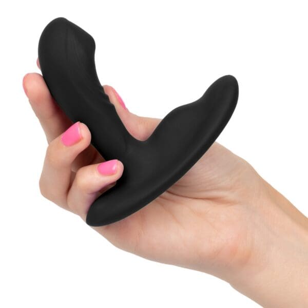 A hand holding a black sex toy in front of a white background.